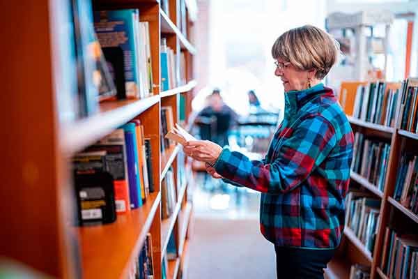 Woman considers book among shelves in library