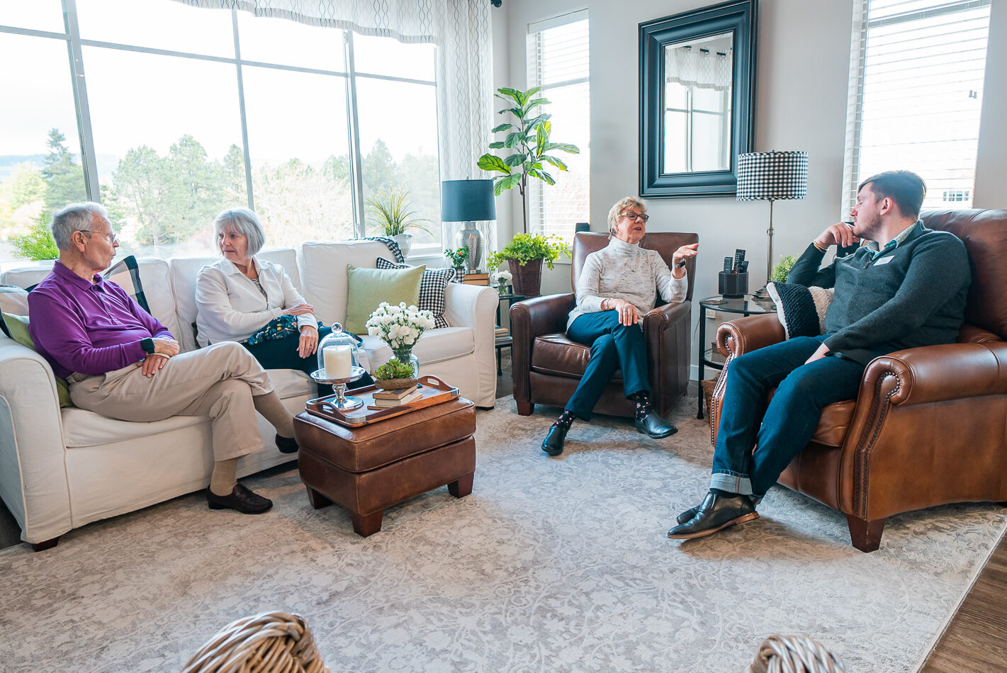 A small group sits in a living room with big windows