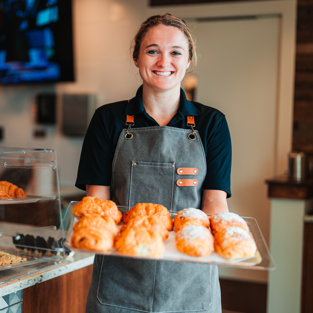 Staff member holding fresh baked pastries and smiling